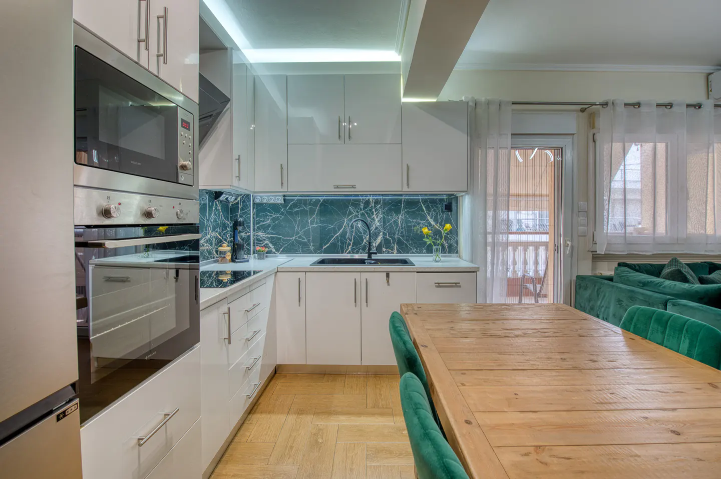 A modern kitchen with white cabinets, a marble backsplash, and a wooden table with green chairs.
