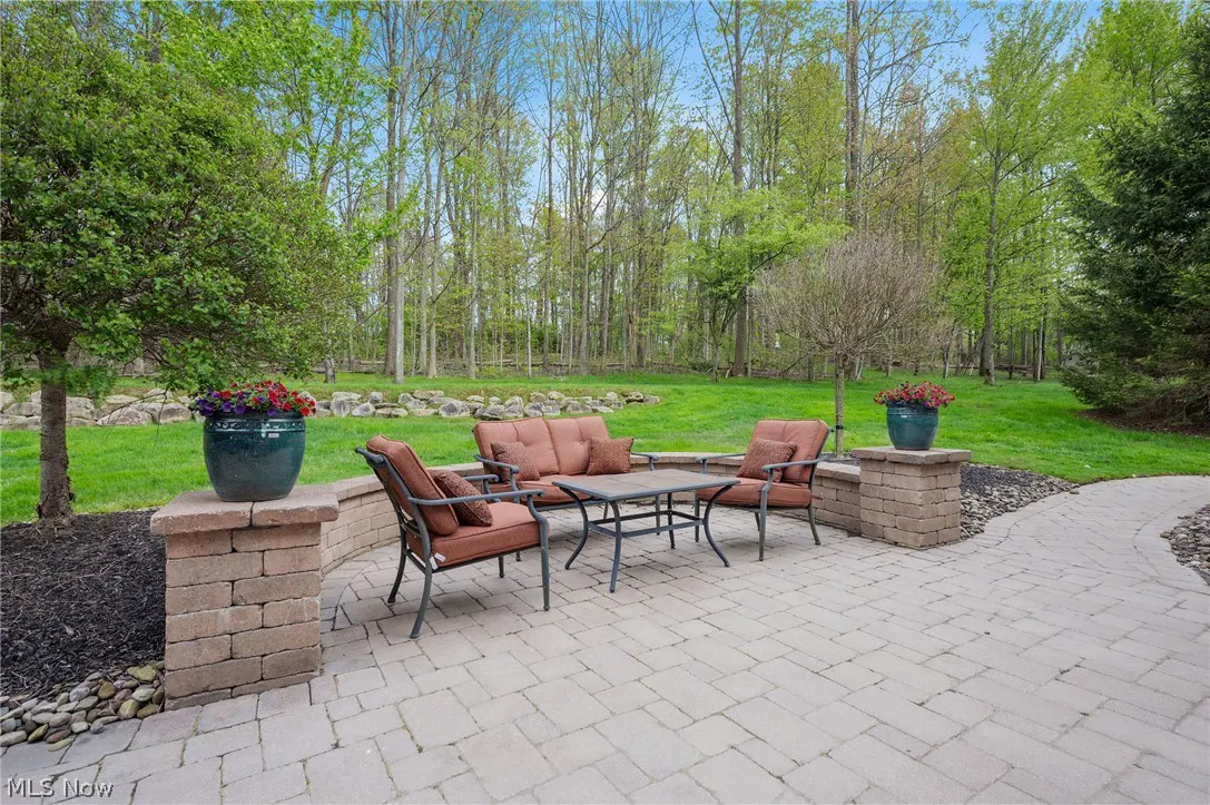 Outdoor patio with brown cushioned seating, a table, and potted flowers, surrounded by green grass and trees.