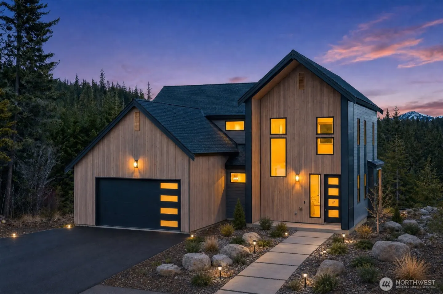 Exterior shot of a modern two-story home with wood siding, a dark roof, and a garage at dusk.