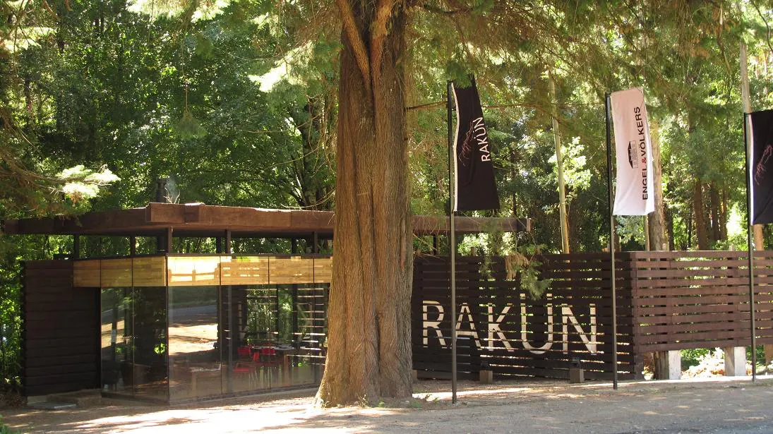 Exterior view of Rakun real estate office with flags and a modern glass building surrounded by trees.