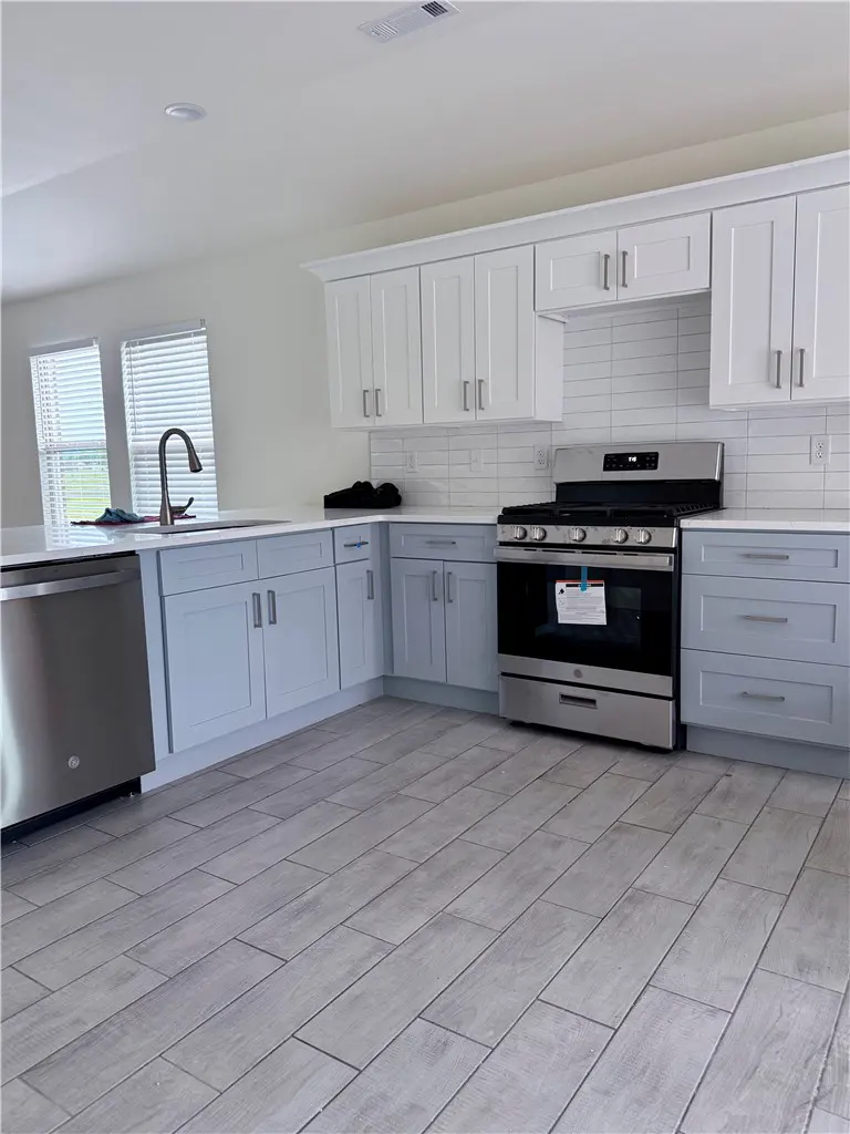 Bright kitchen with white upper cabinets, light blue lower cabinets, stainless steel appliances, and gray wood-look tile flooring.