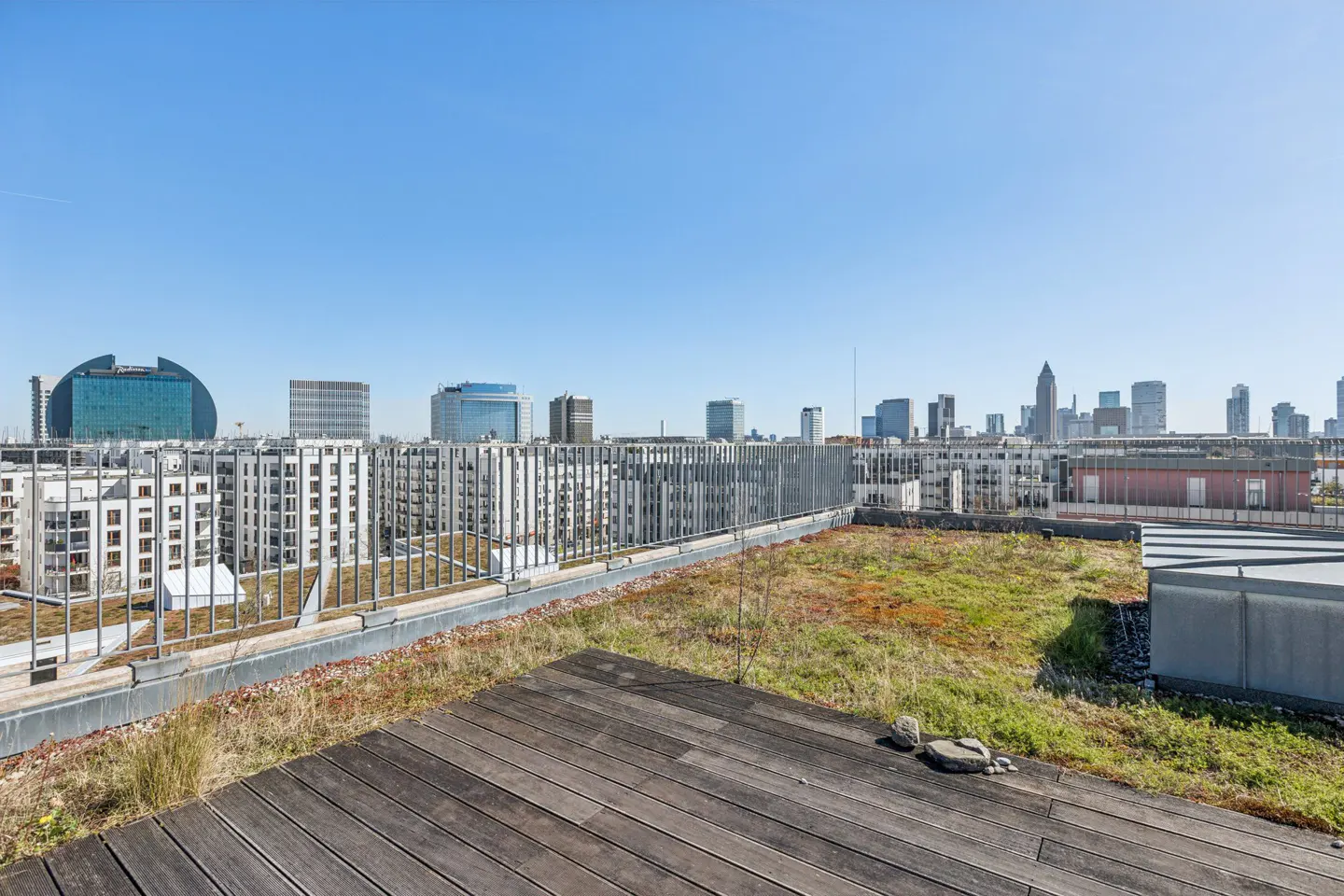 Rooftop view of Frankfurt, Germany, with a wooden deck, green roof, and city skyline under a clear blue sky.