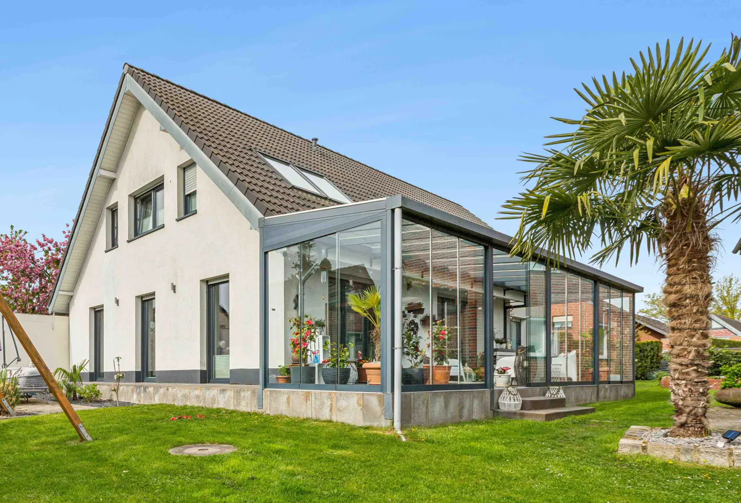 A white house with a glass sunroom extension and a palm tree in the yard.