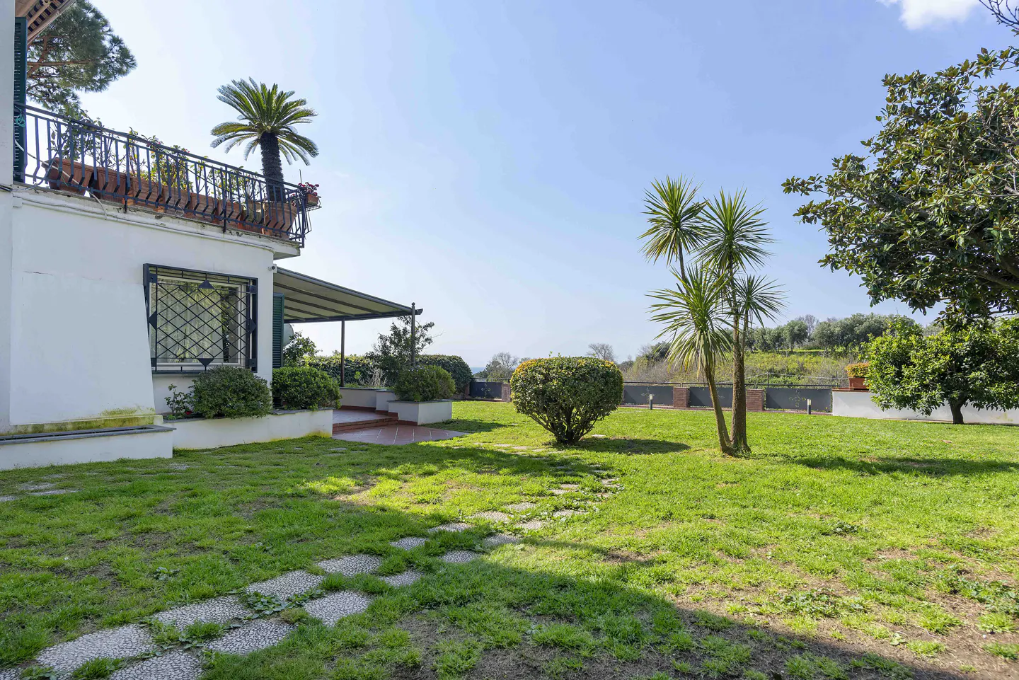 Exterior view of a white house with a green lawn, trees, and a stone pathway under a blue sky.