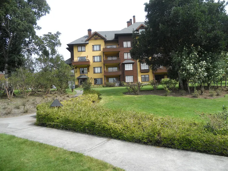 A three-story apartment building with yellow and brown siding, balconies, and a green lawn.