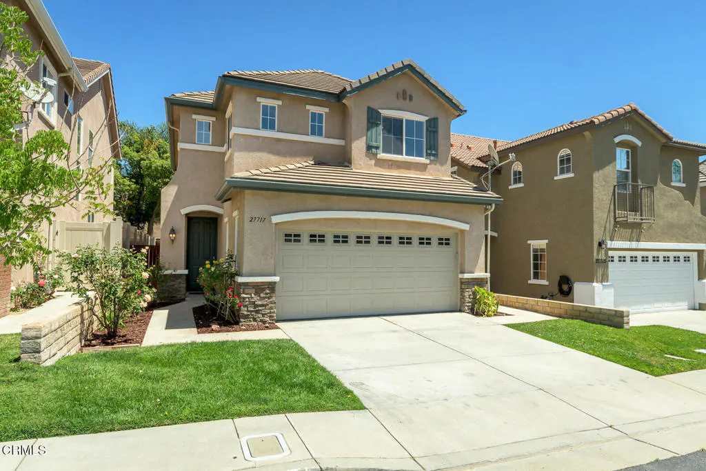 Two-story beige house with a green door, a two-car garage, and a concrete driveway on a sunny day.