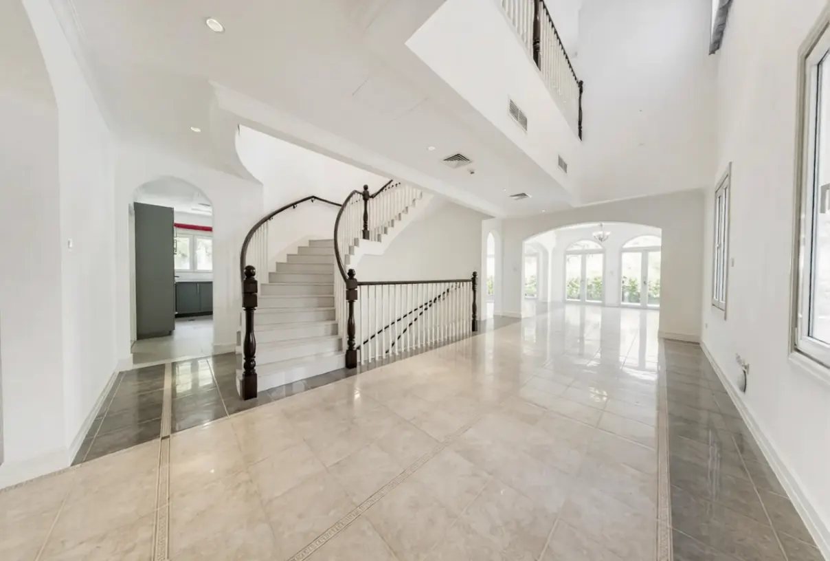 Bright, open foyer with a curved staircase, white walls, and tiled floors. Arched doorways lead to other rooms. Natural light streams in.