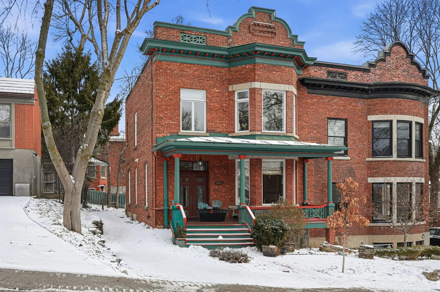A three-story red brick house with green trim and a snow-covered yard on a sunny day.