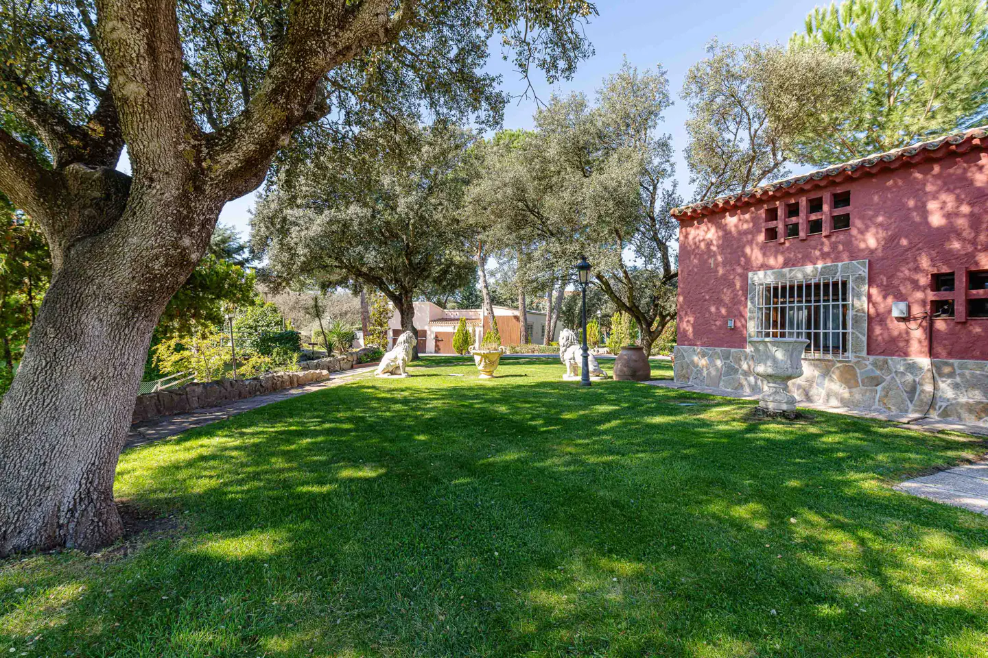 Lush green lawn with trees, lion statues, and a red building with stone accents under a blue sky.