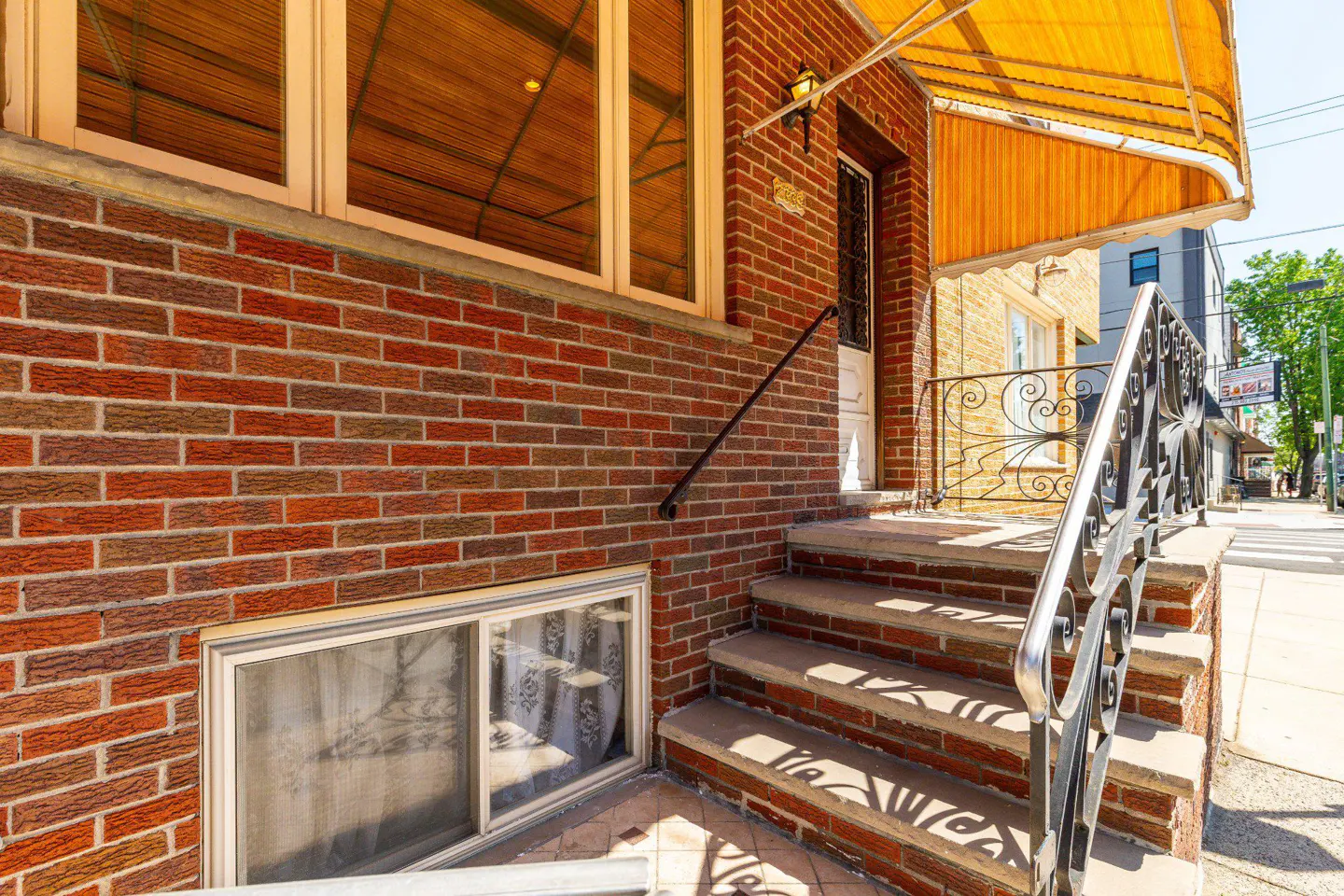 Exterior view of a red brick house with concrete steps, a metal railing, and a yellow awning.
