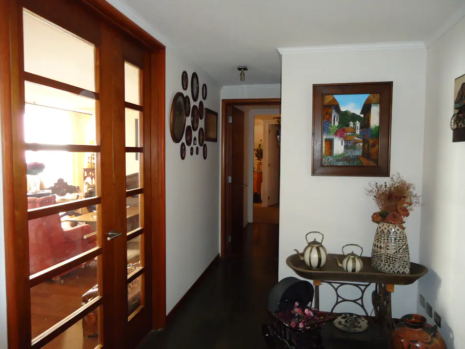 Hallway with dark wood floors, white walls, and wood-framed glass doors. Artwork and decorative items adorn the walls and a table.