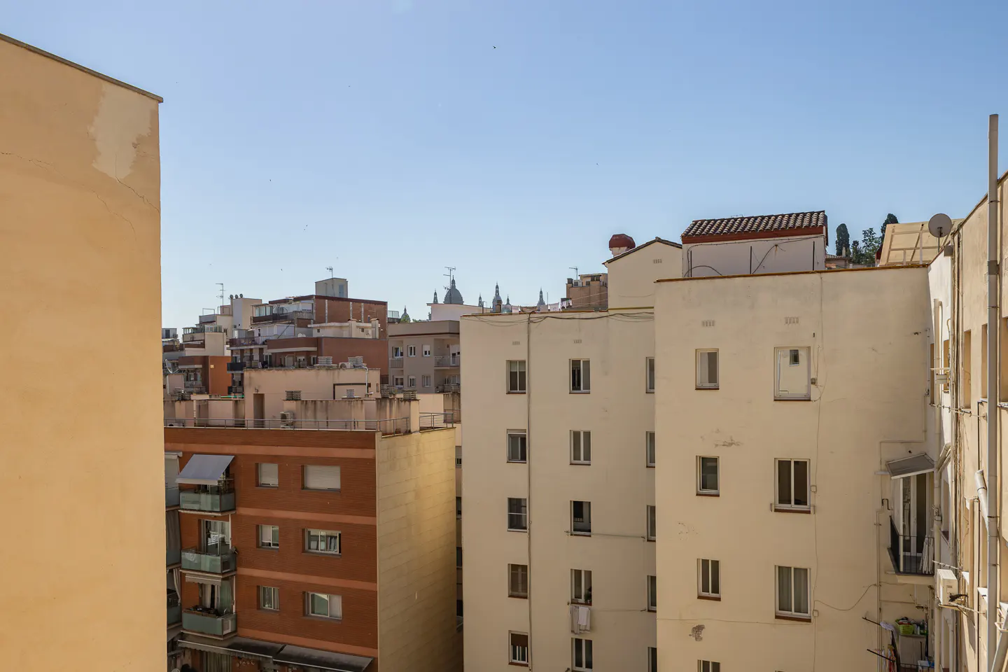View of apartment buildings in a city, with a clear blue sky above. Buildings are tan, brown, and white.