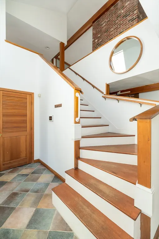 Interior view of a home foyer with wood stairs, white walls, and a multi-colored tile floor. A wood door is on the left.