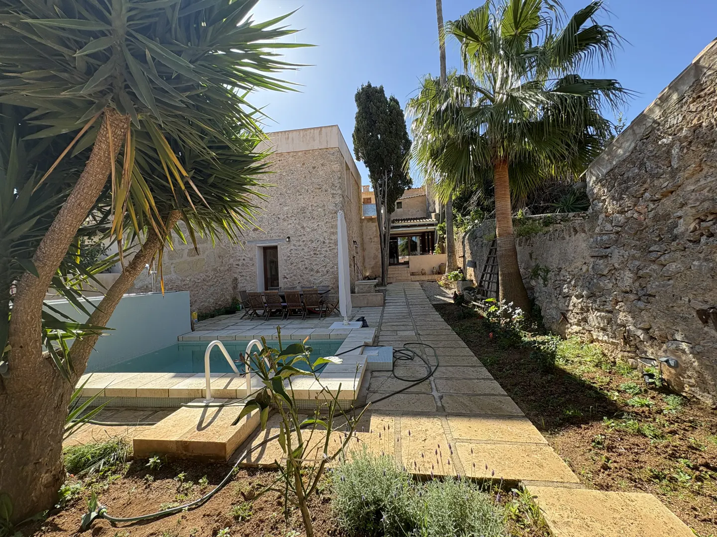 Exterior view of a stone house with a pool, palm trees, and a stone pathway leading to the house.
