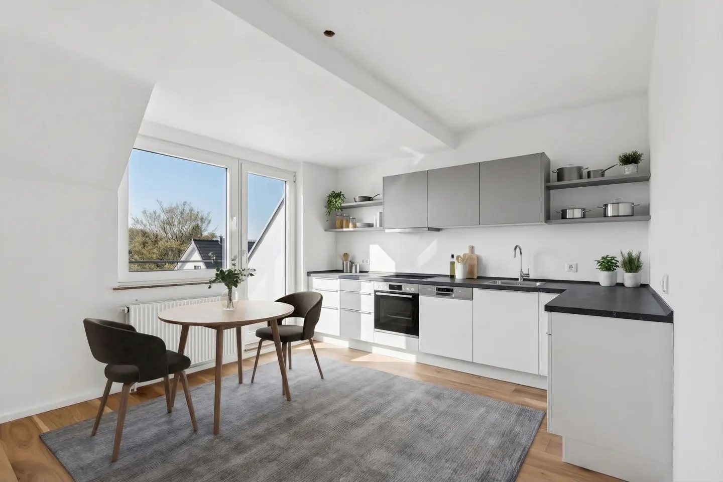 Bright kitchen with white cabinets, gray countertops, and a round wooden table with two chairs on a gray rug.