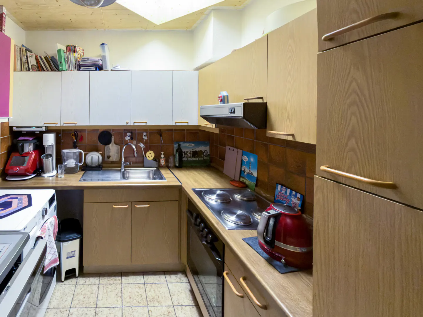 A kitchen with white cabinets, brown backsplash, and wood cabinets. A red kettle sits on the counter next to a stove.