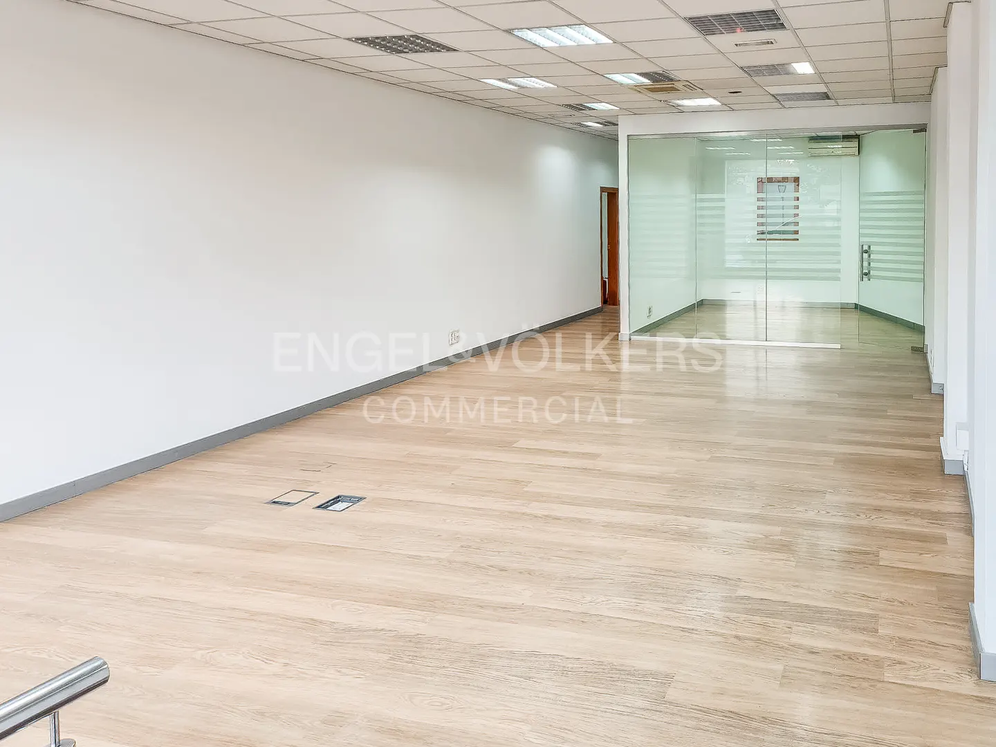 Bright, empty office space with wood floors, white walls, and a glass-enclosed room at the end.