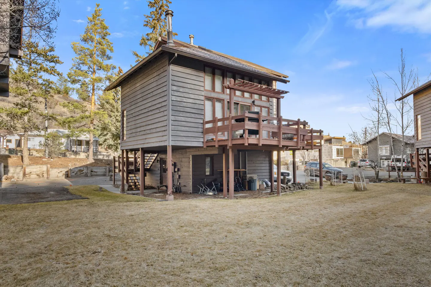 Exterior view of a two-story gray house on stilts with a brown deck and a chimney, set against a blue sky.