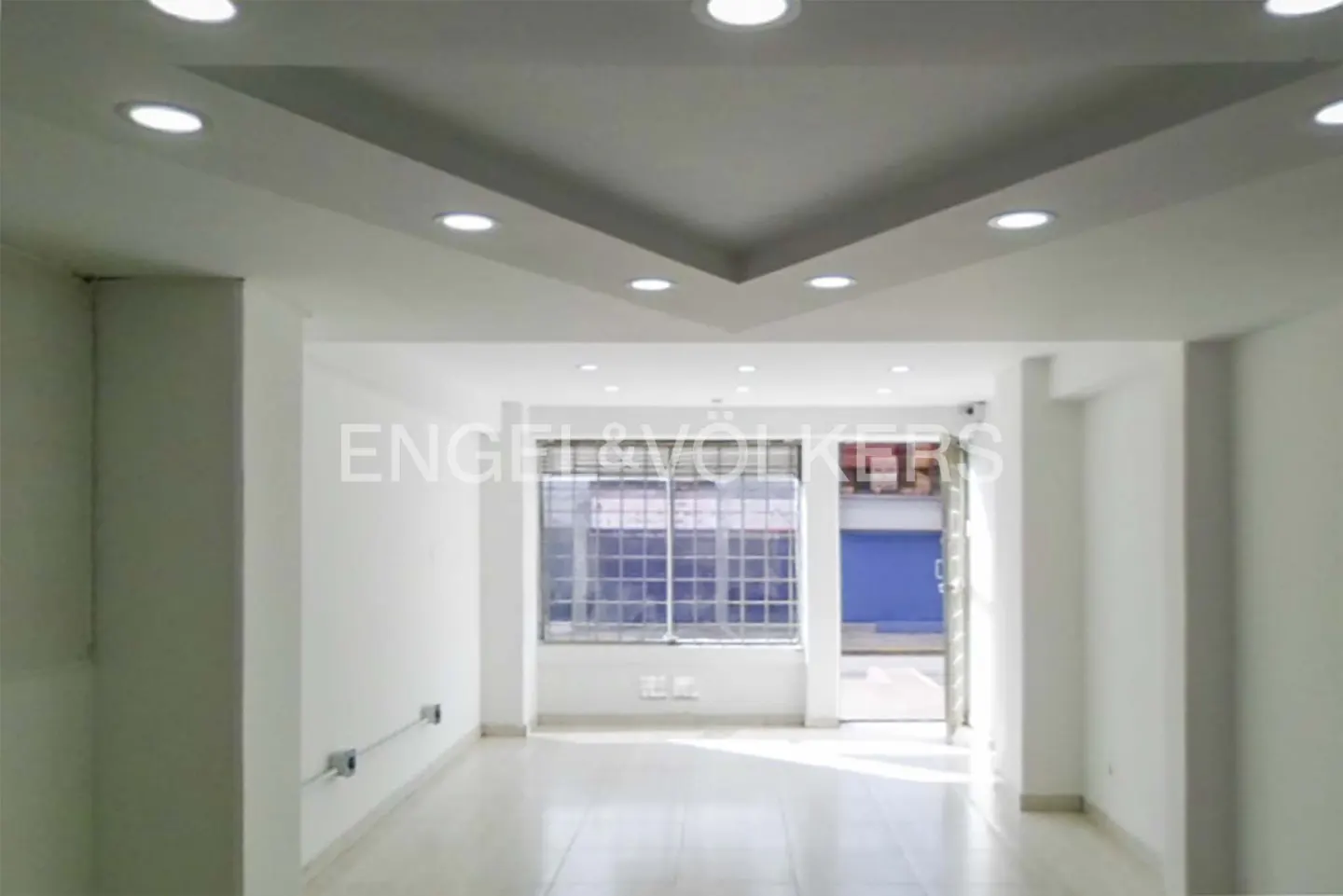 Empty white commercial space with recessed lighting, large window, and Engel & Völkers logo.