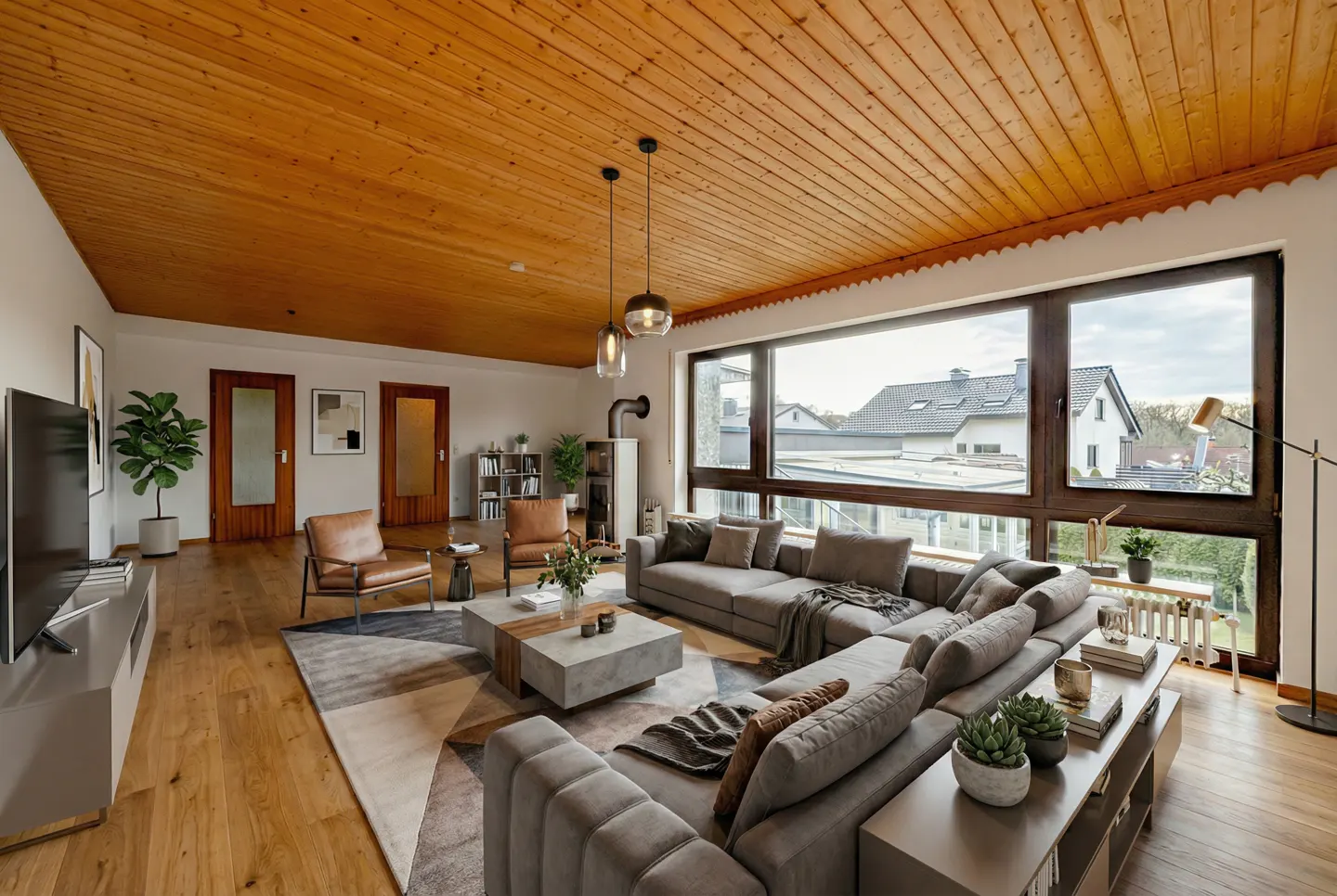 Modern living room with wood-paneled ceiling, large windows, gray sectional sofa, two leather chairs, and a coffee table.
