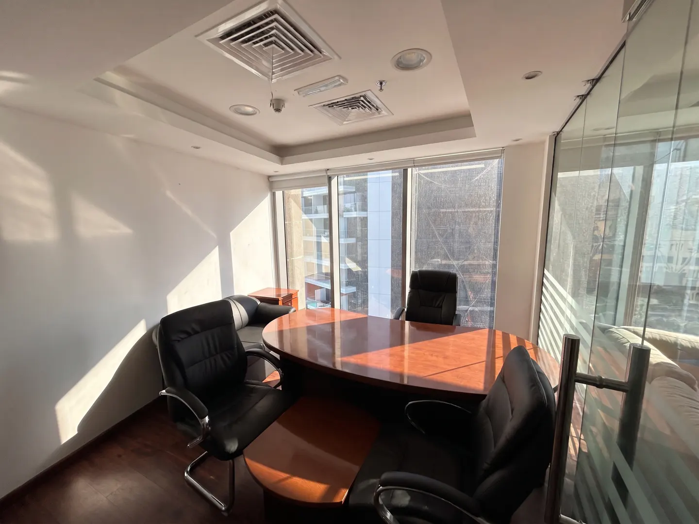 Office space with a large wood desk, black leather chairs, and floor-to-ceiling windows with city views.