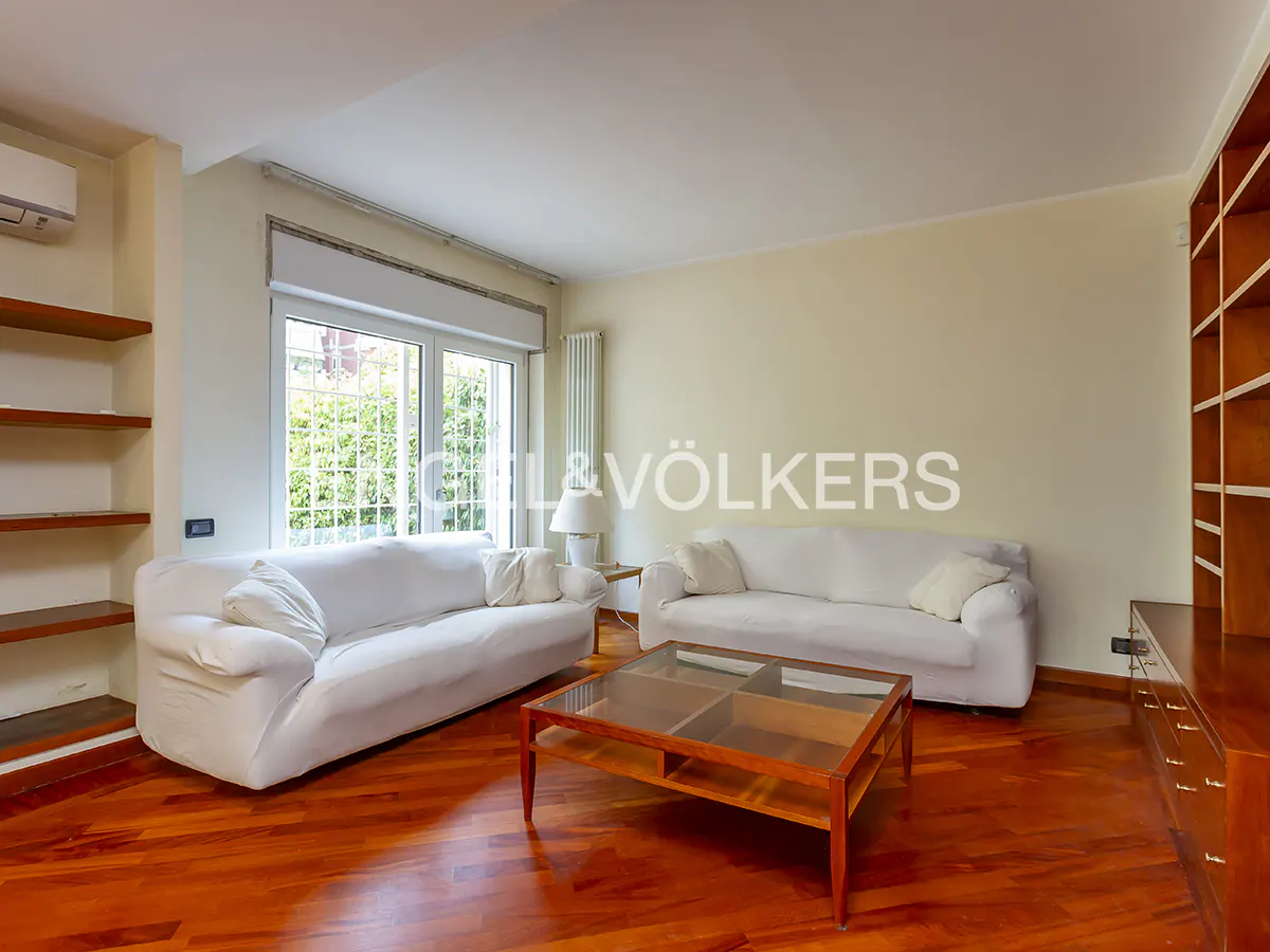 Living room with two white sofas, a wooden coffee table, and a large window overlooking a green garden.
