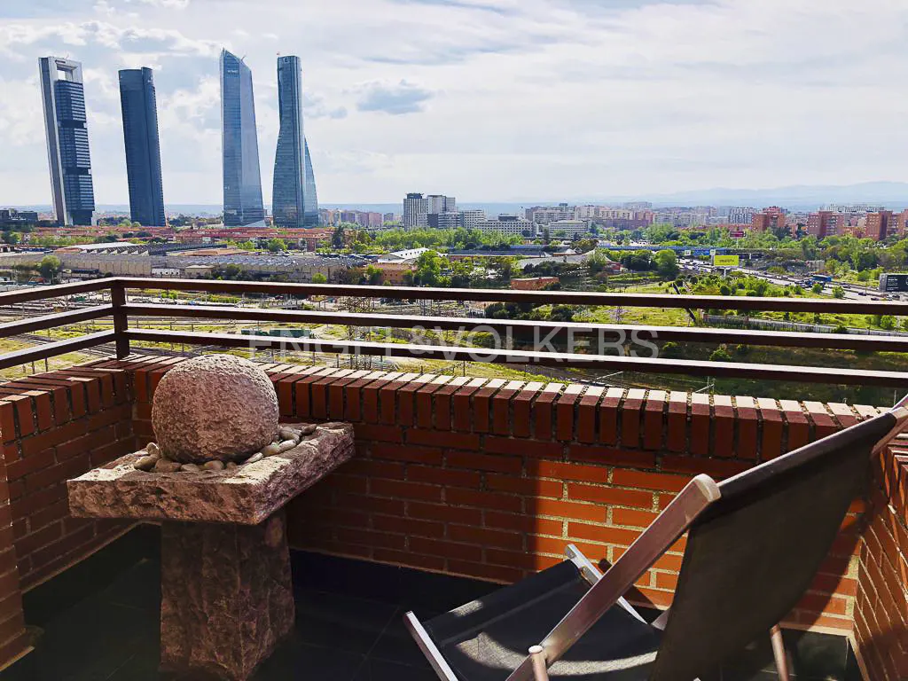 Balcony view of Madrid skyline with four skyscrapers. A stone table and chair sit on the brick-walled balcony.