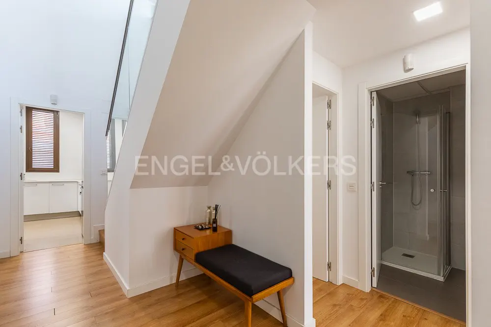 Hallway with wood floors, white walls, and a glass-railed staircase. A bench sits under the stairs, and a bathroom is visible.