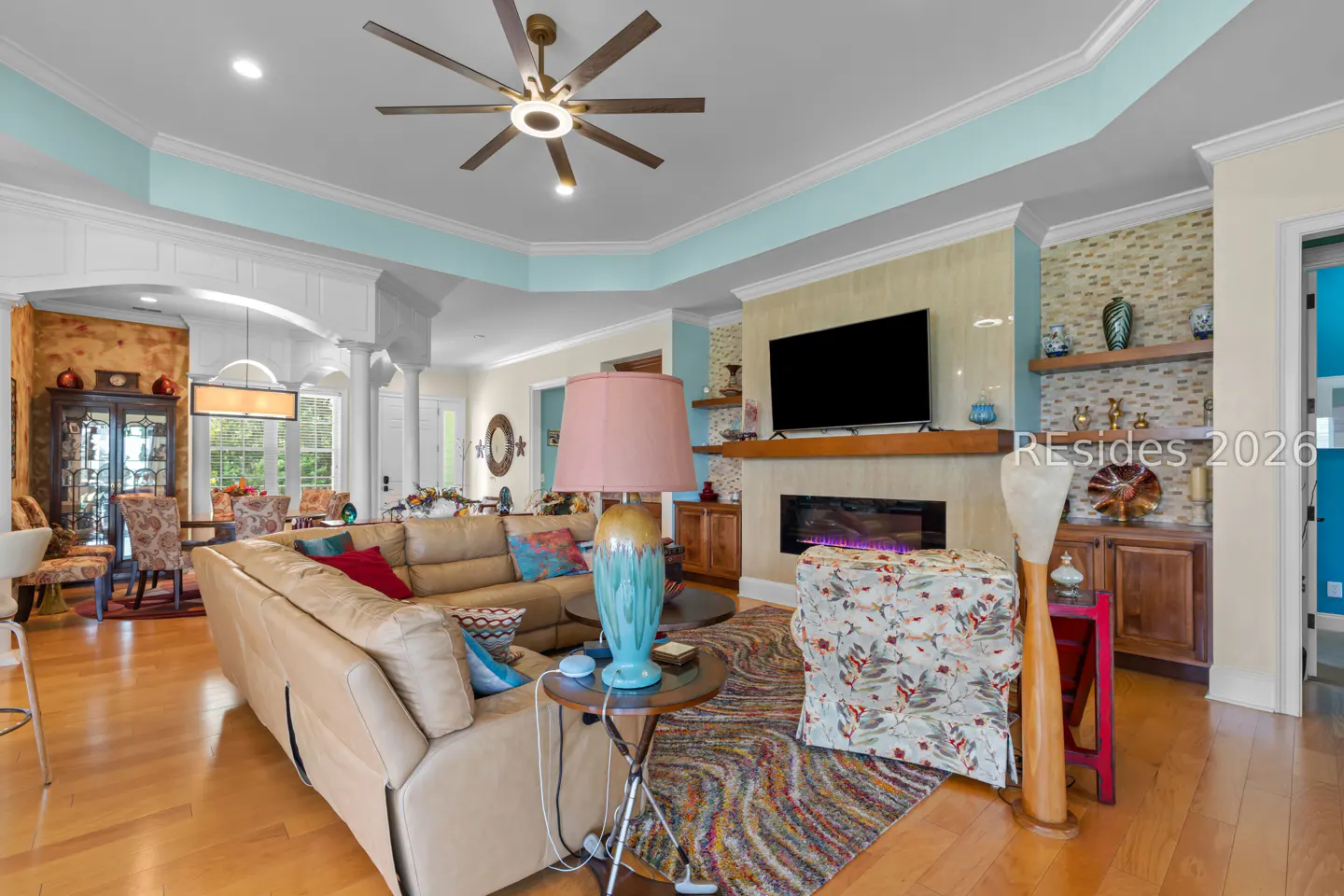 A living room with a tan leather sofa, a blue lamp, a fireplace, and a ceiling fan.