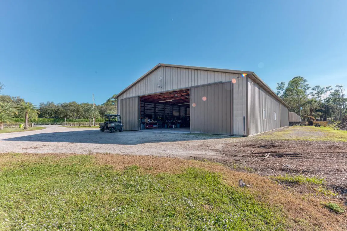 A large, open metal barn with a dark green utility vehicle parked outside on a sunny day.