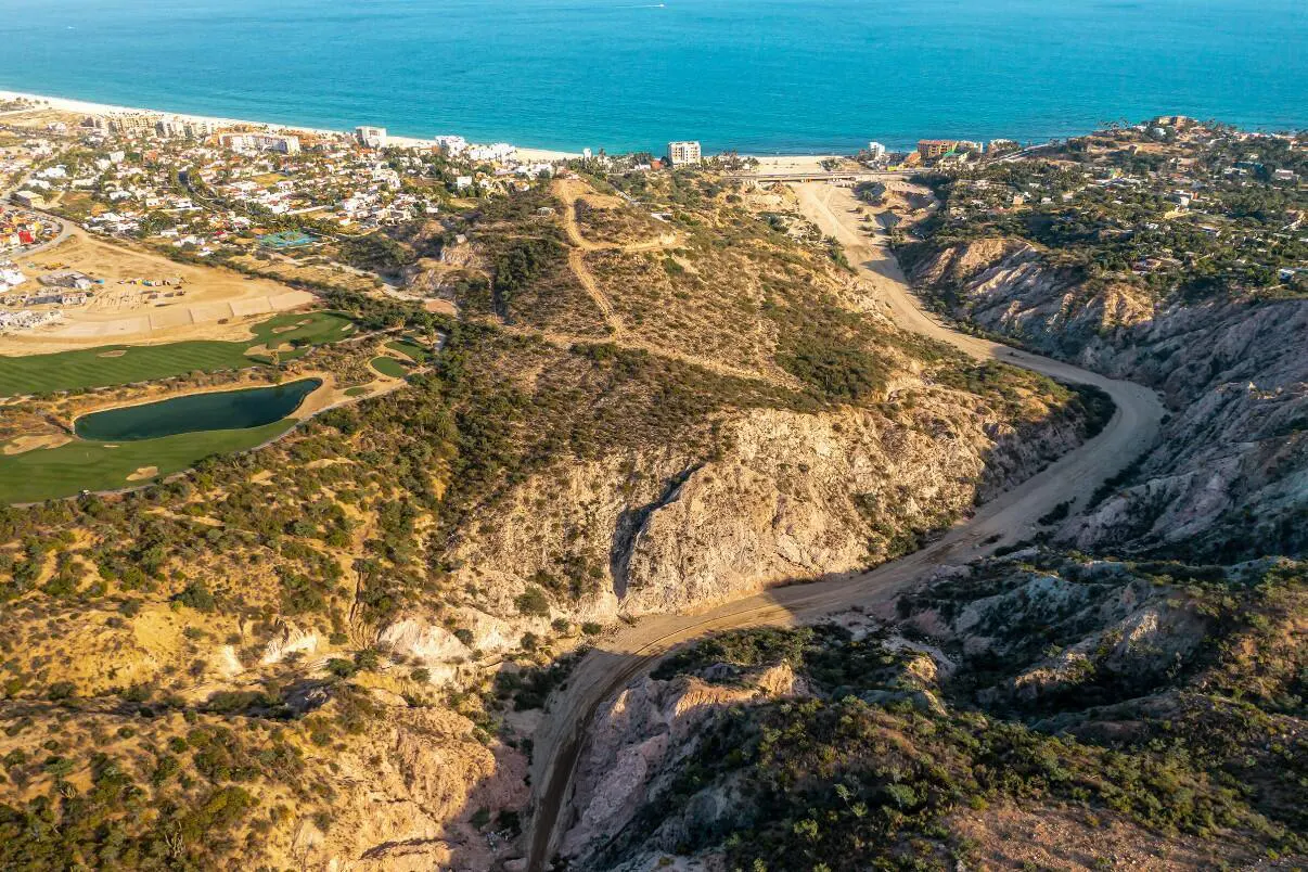 Aerial view of a desert landscape with a winding dirt road leading to a coastal city and the blue ocean.