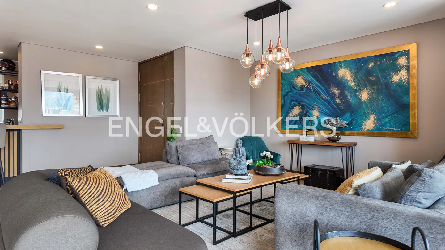 Living room with gray sofas, wood tables, and a blue and gold abstract painting. A modern light fixture hangs above the coffee table.