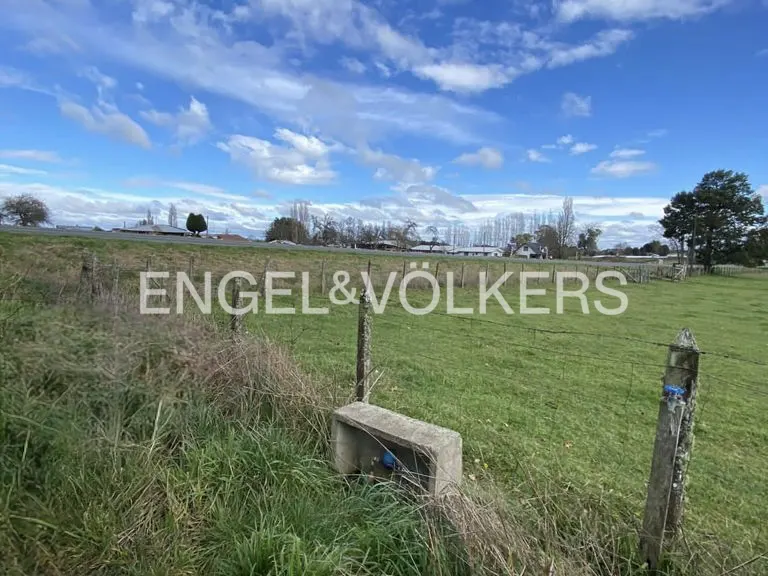 Green field with a barbed wire fence under a blue sky with clouds. Engel & Völkers logo overlay.