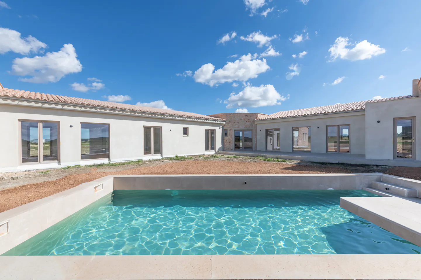 A modern home with a pool. The house is white with a red tile roof. The pool is turquoise and has a diving board. Blue sky with clouds.
