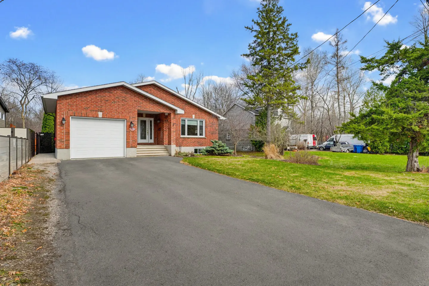 Single-story red brick house with a white garage door, asphalt driveway, and green lawn under a blue sky.