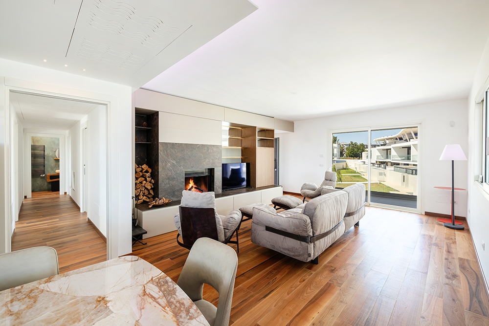 Modern living room with hardwood floors, a fireplace, grey sofa, and large sliding doors opening to a patio.