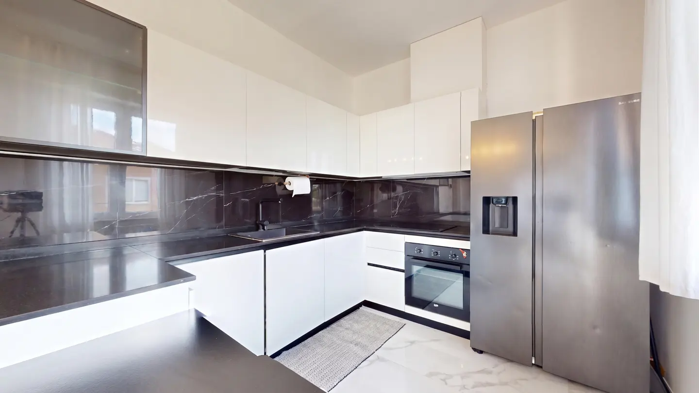 Modern kitchen with white cabinets, black marble backsplash, stainless steel refrigerator, and white marble-look flooring.