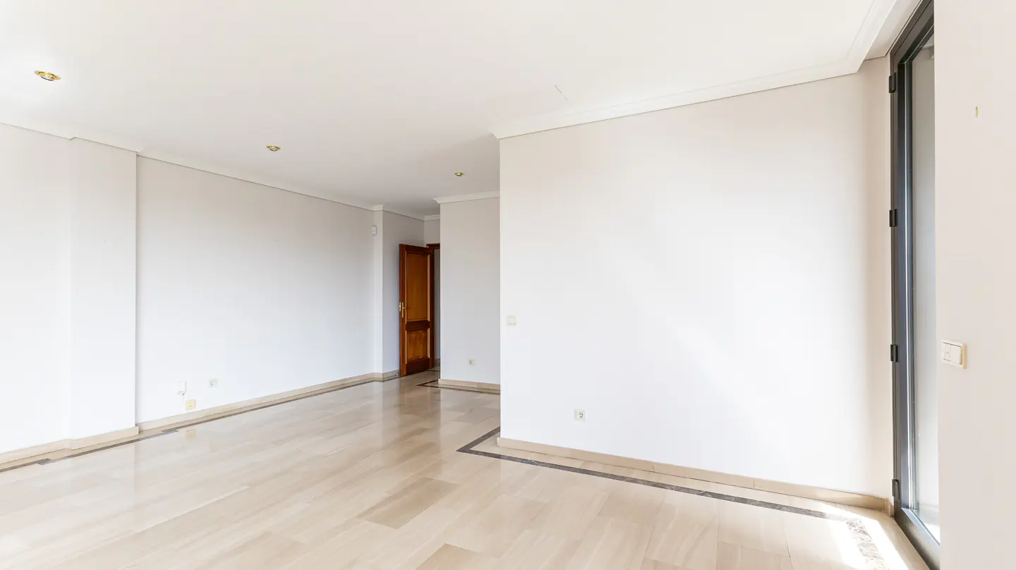 Empty room with white walls, marble floors, and a dark wood door in the background. A black-framed window is on the right.