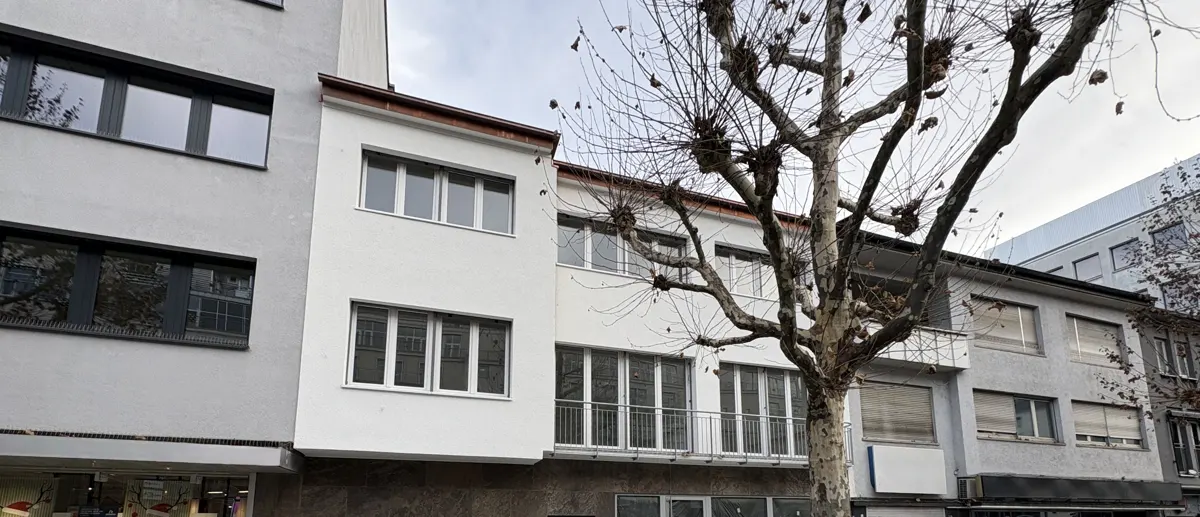Exterior view of a multi-story building with white facade and multiple windows, next to a bare tree.