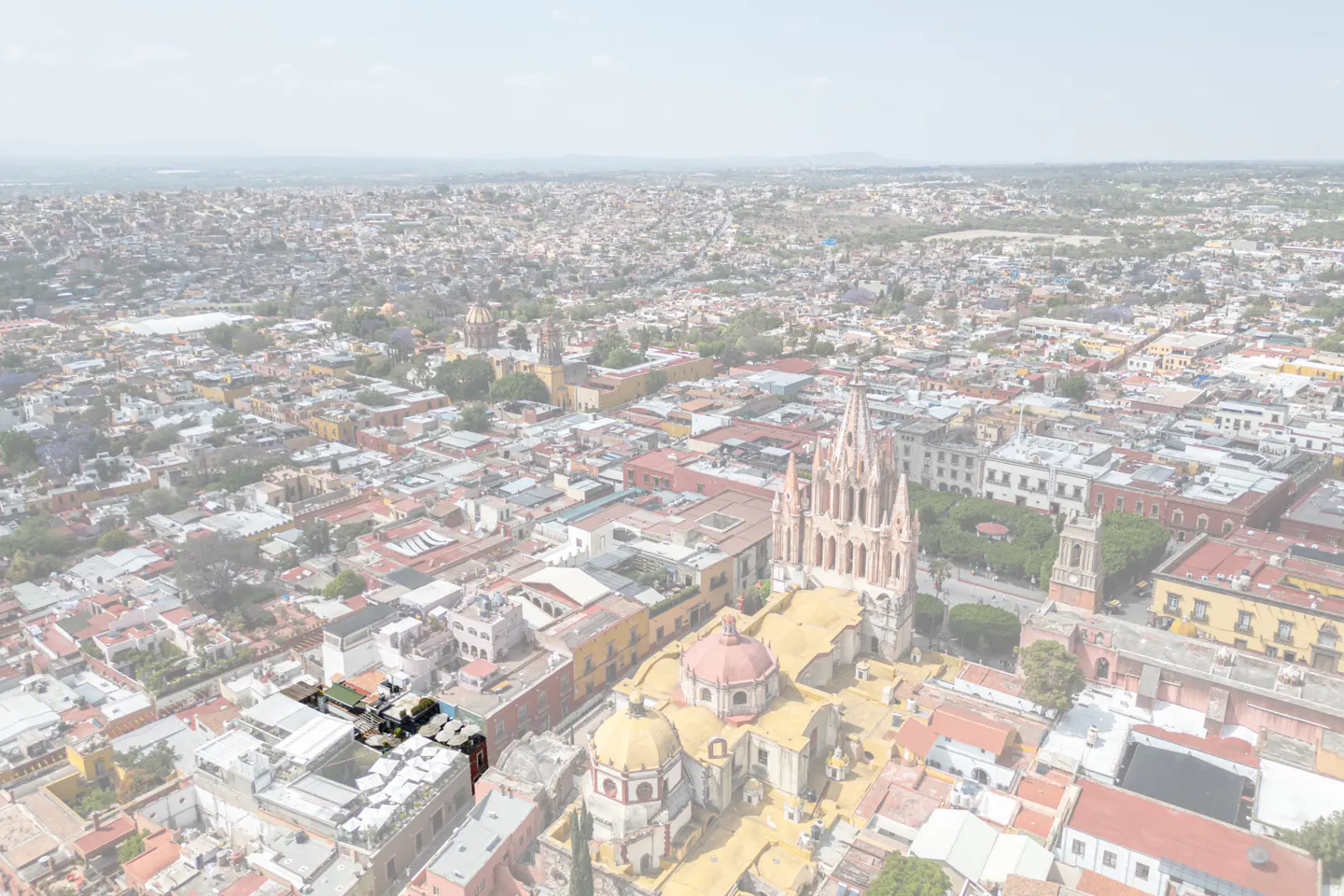 Aerial view of San Miguel de Allende, Mexico, featuring colonial architecture and a prominent church with tall spires.
