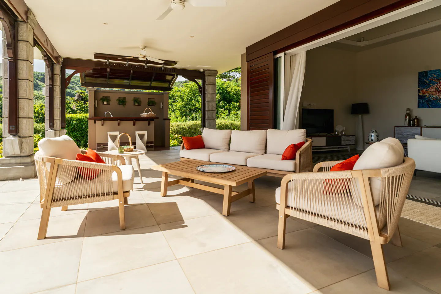 Outdoor patio with a beige sofa, two chairs with orange pillows, and a wooden coffee table. A bar area is in the background.