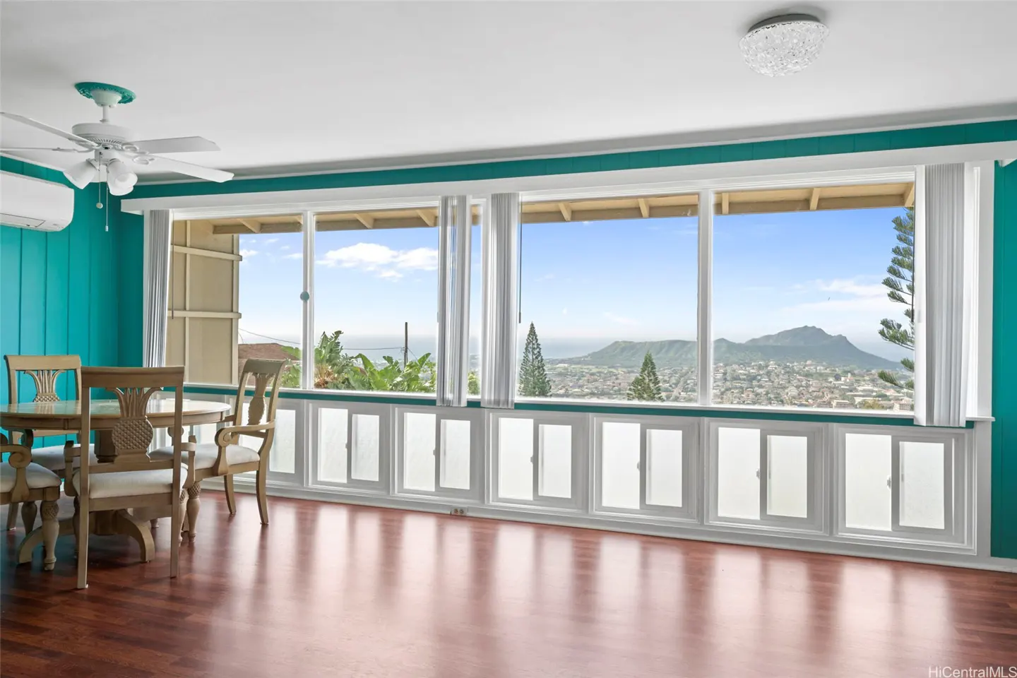 Bright room with wood floors, turquoise walls, and a large window view of Diamond Head. A dining table and chairs are visible.