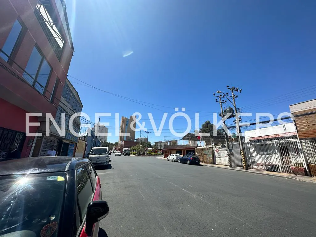 Street view with cars parked along the sides, buildings, and a clear blue sky.