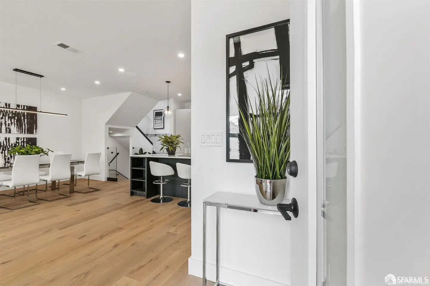 A bright, modern home interior with a dining area, kitchen, and a console table with a plant near the entrance.