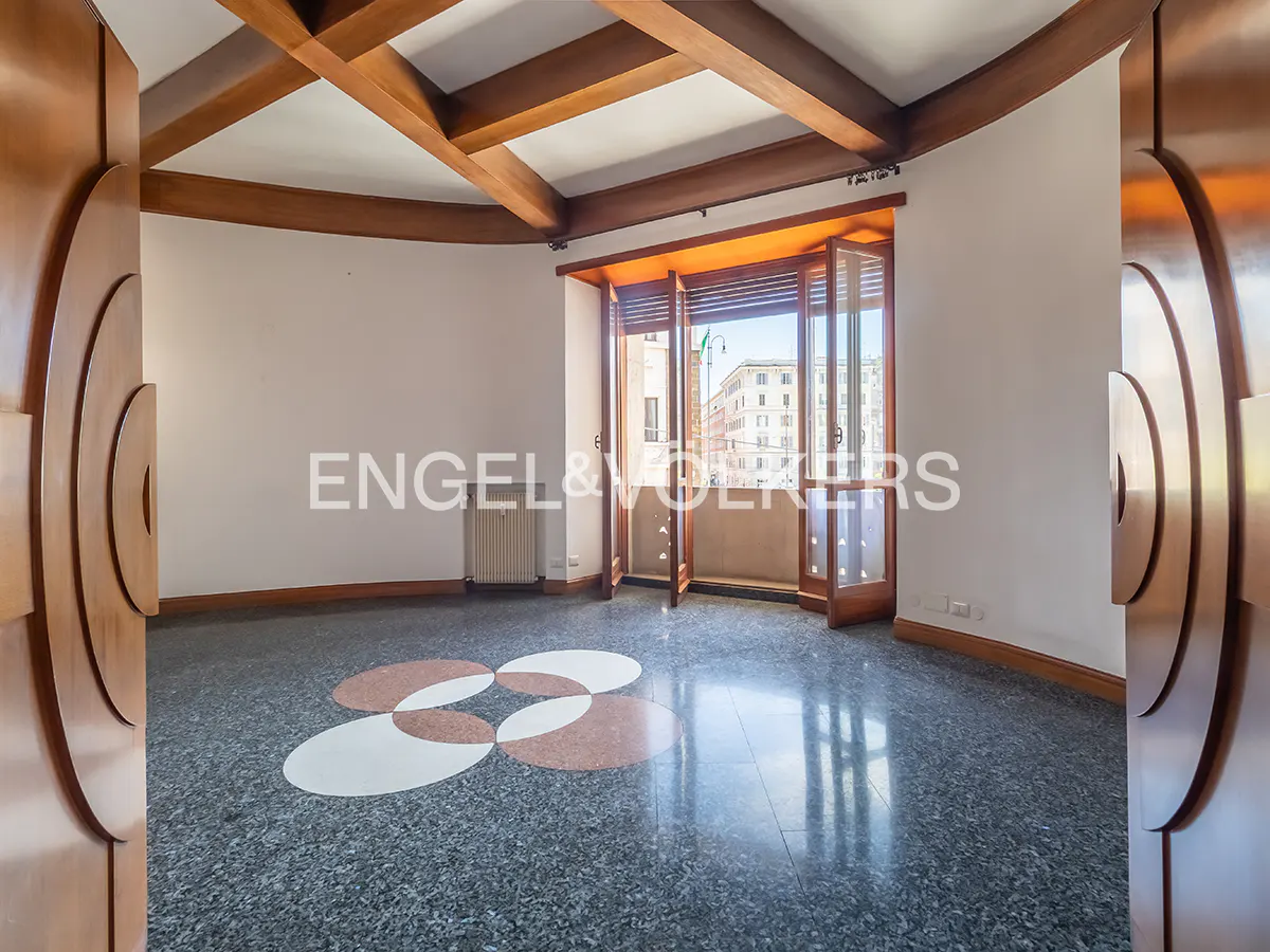 An empty room with a wooden beamed ceiling, a terrazzo floor with a flower pattern, and an open balcony door.