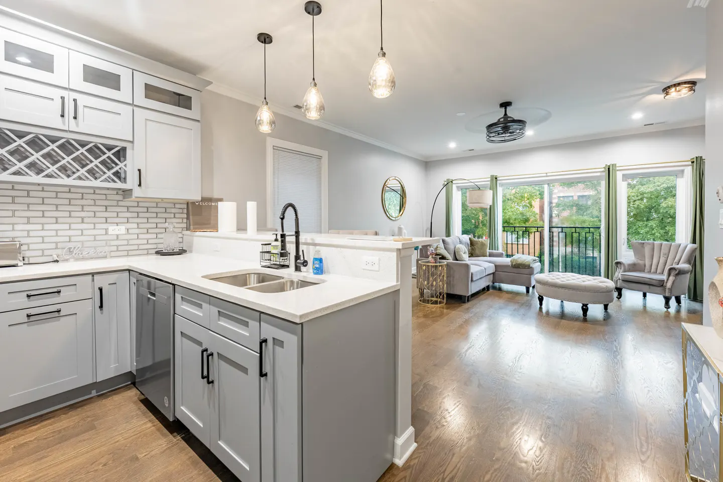 Open concept living space with gray cabinets, white countertops, and a living room with a gray sofa and balcony.