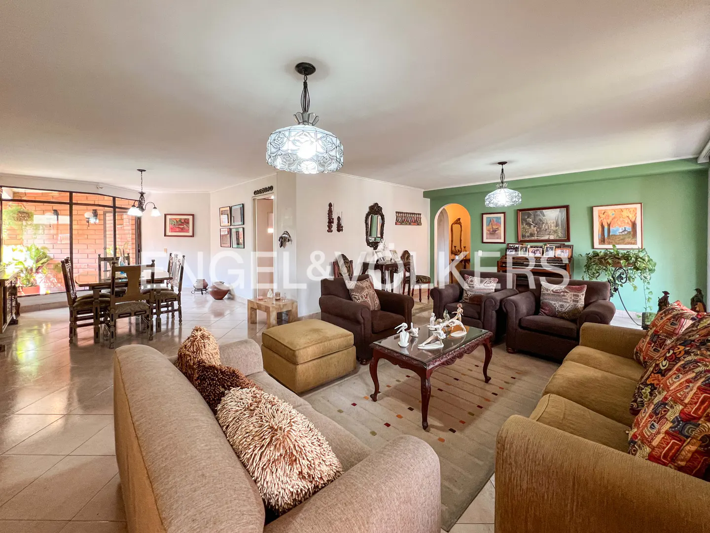 Open-concept living and dining room with brown sofas, chairs, and a dining table. A green accent wall adds color to the space.