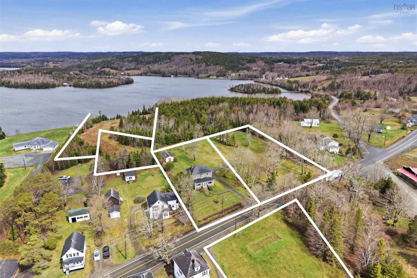 Aerial view of a property with white boundary lines, near a lake and forest under a blue sky.