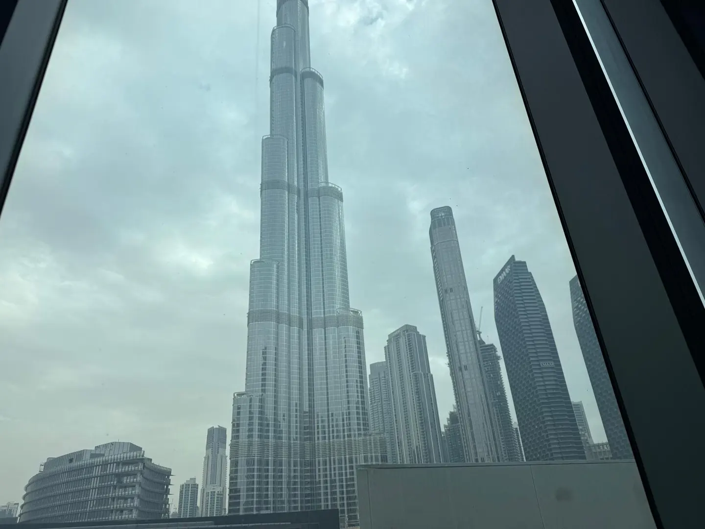 View of the Burj Khalifa and Dubai skyline through a window on a cloudy day.