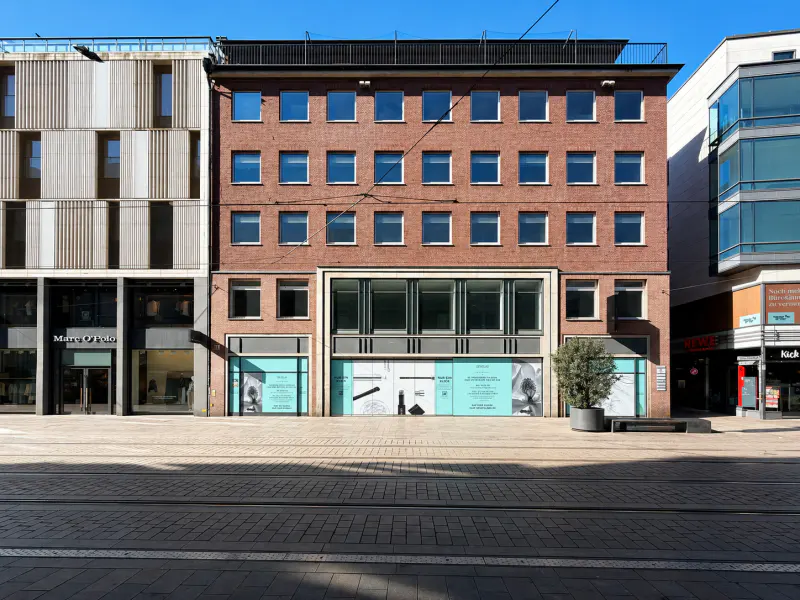 Exterior of a brick building with large windows on a sunny day. A paved street runs in front of the building.